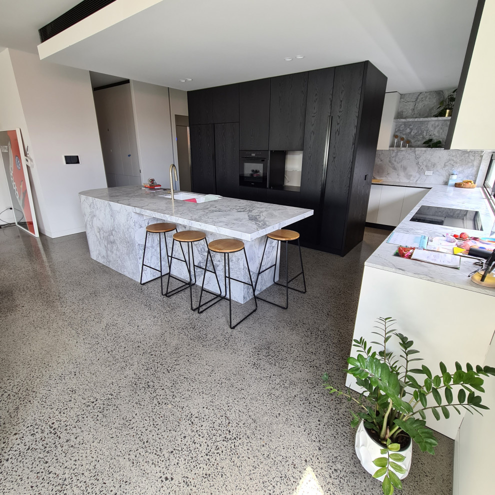 Inspiration for a large contemporary u-shaped open plan kitchen in Melbourne with an undermount sink, flat-panel cabinets, black cabinets, marble benchtops, window splashback, stainless steel appliances, concrete floors, with island, grey floor and white benchtop.