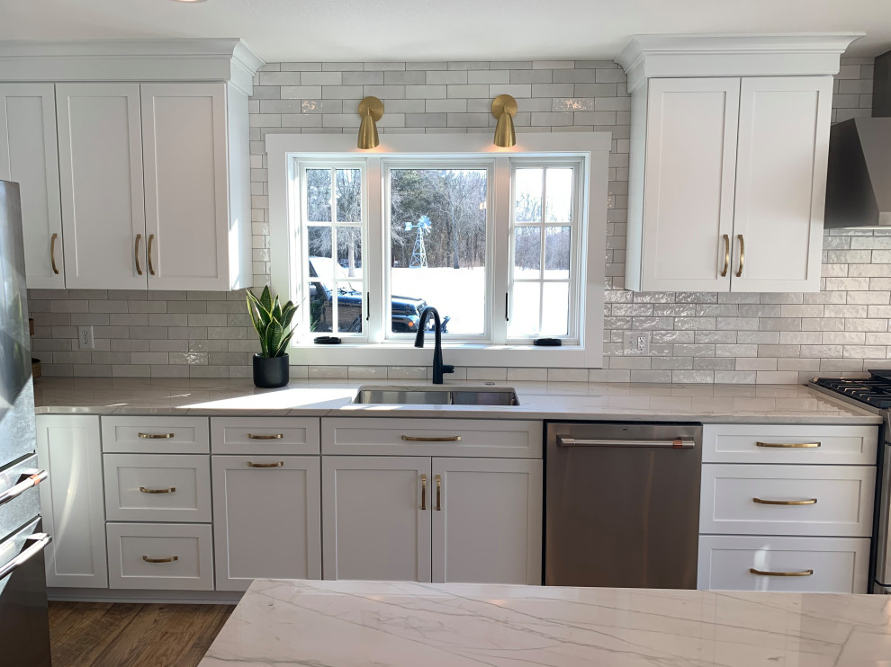 Example of a large transitional l-shaped vinyl floor and brown floor eat-in kitchen design with an undermount sink, shaker cabinets, white cabinets, quartz countertops, stainless steel appliances, an island and gray countertops