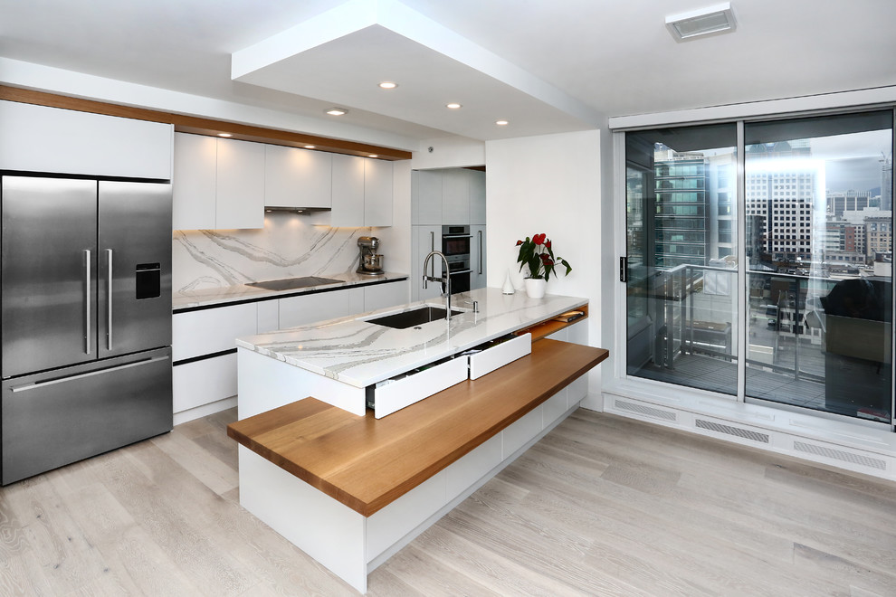 This is an example of a small contemporary galley eat-in kitchen in Vancouver with a drop-in sink, flat-panel cabinets, white cabinets, granite benchtops, white splashback, porcelain splashback, stainless steel appliances, light hardwood floors, with island and grey floor.