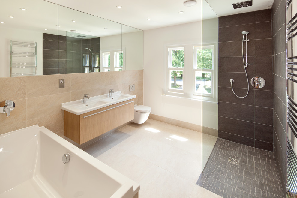 This is an example of a large contemporary bathroom in Oxfordshire with a console sink, flat-panel cabinets, light wood cabinets, a freestanding tub, an open shower, a wall-mount toilet, black tile, stone slab, white walls and porcelain floors.