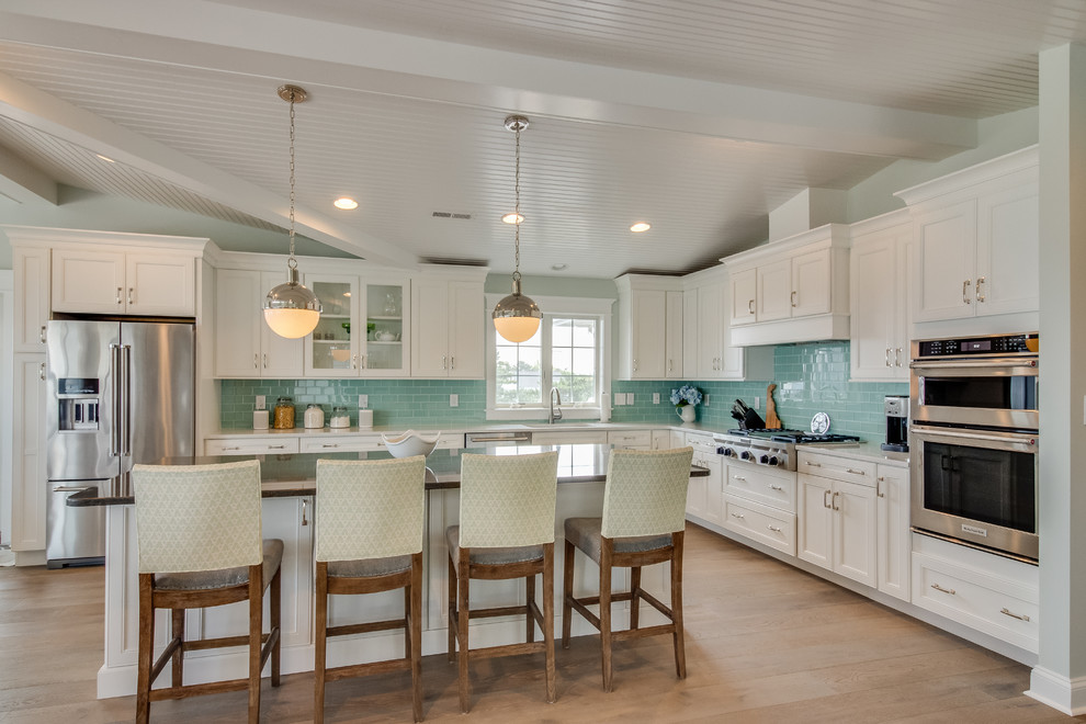 This is an example of a beach style l-shaped kitchen in Other with shaker cabinets, white cabinets, blue splashback, subway tile splashback, stainless steel appliances, medium hardwood floors, with island and brown floor.