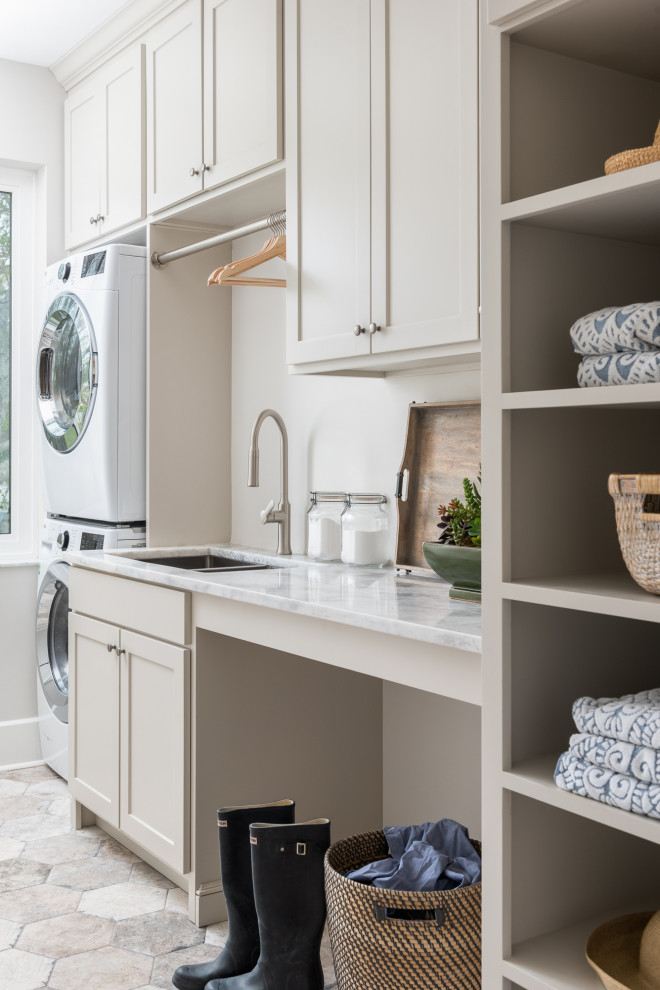 Mid-sized country single-wall dedicated laundry room in Tampa with an undermount sink, shaker cabinets, beige cabinets, marble benchtops, white walls, porcelain floors, a stacked washer and dryer, beige floor and white benchtop.