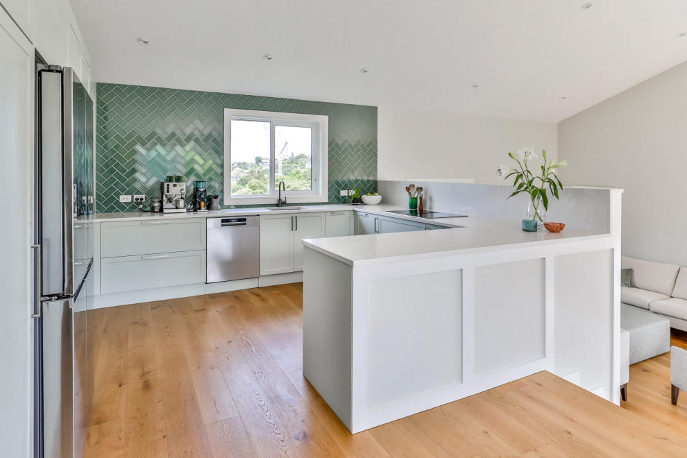 This is an example of a Mid-sized contemporary U-shaped eat-in kitchen in Auckland With an Undermount Sink, Shaker Cabinets, Green Cabinets, Quartz Benchtops, Green Splashback, Subway Tile Splashback, Stainless Steel Appliances, Medium Hardwood Floors, a Peninsula, Brown Floor, White Benchtop and Vaulted.