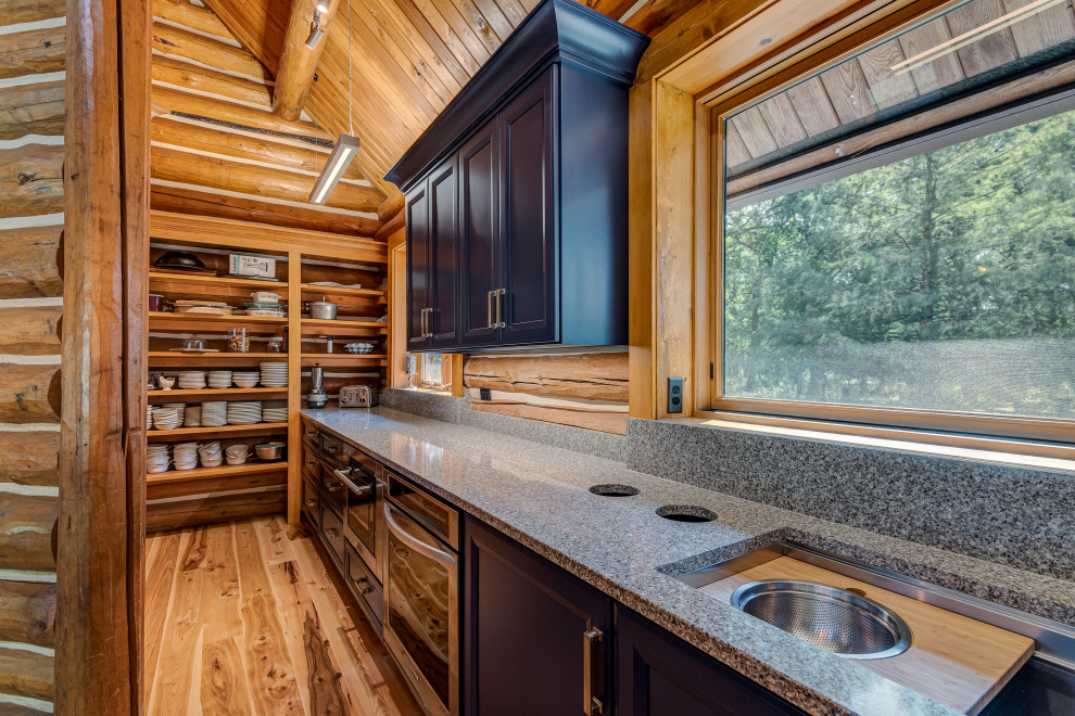 Cette image montre une cuisine américaine parallèle traditionnelle avec un évier encastré, un placard à porte shaker, des portes de placard bleues, un plan de travail en quartz, une crédence en bois, un électroménager en acier inoxydable, un sol en bois brun, îlot et un plan de travail gris.