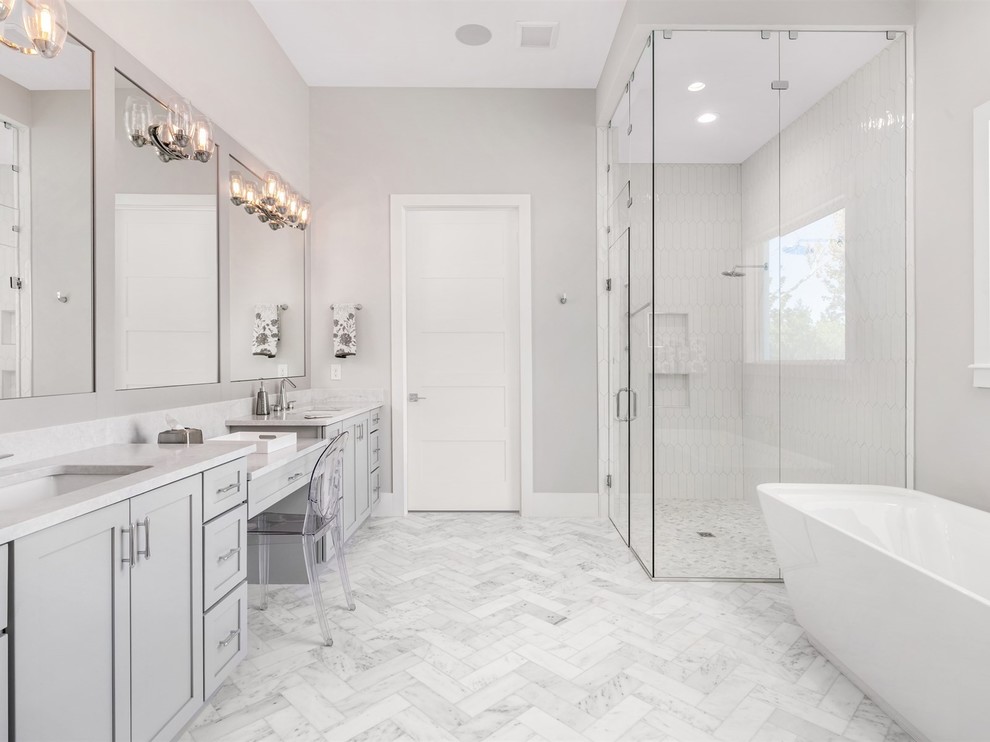 Inspiration for a mid-sized transitional master bathroom in Orlando with shaker cabinets, grey cabinets, a freestanding tub, a corner shower, a two-piece toilet, grey walls, an undermount sink, grey floor, a hinged shower door, white benchtops, white tile, marble floors and engineered quartz benchtops.