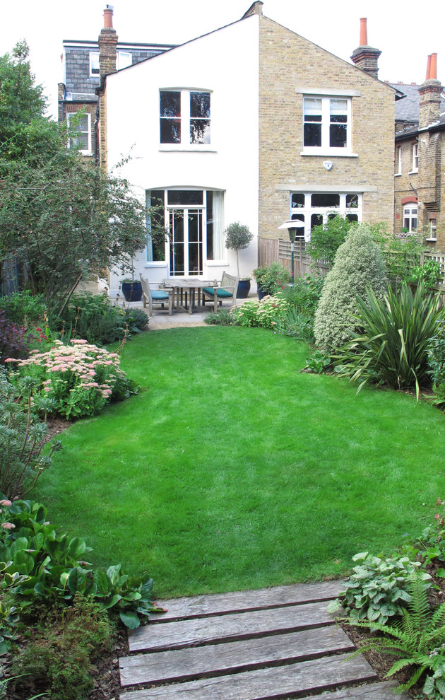 Large traditional backyard full sun garden in London with natural stone pavers for summer.