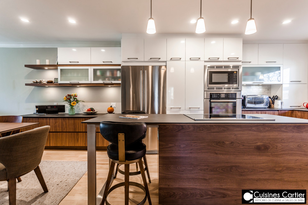 Large transitional galley medium tone wood floor eat-in kitchen photo in Montreal with an undermount sink, flat-panel cabinets, dark wood cabinets, quartzite countertops, white backsplash, mosaic tile backsplash, stainless steel appliances and an island