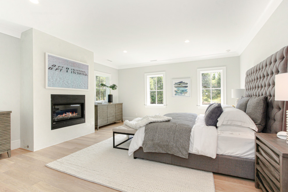 This is an example of a mid-sized contemporary master bedroom in New York with white walls, light hardwood floors, a hanging fireplace, a concrete fireplace surround and beige floor.