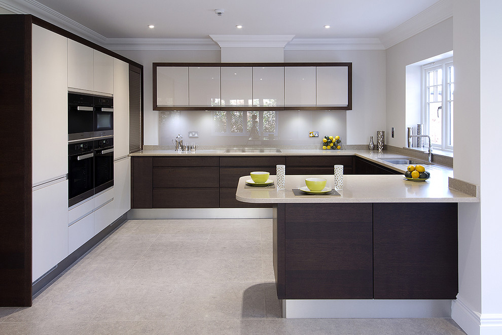 Inspiration for a mid-sized contemporary u-shaped open plan kitchen in Buckinghamshire with a drop-in sink, flat-panel cabinets, beige cabinets, quartzite benchtops, metallic splashback, glass sheet splashback, black appliances, limestone floors and with island.