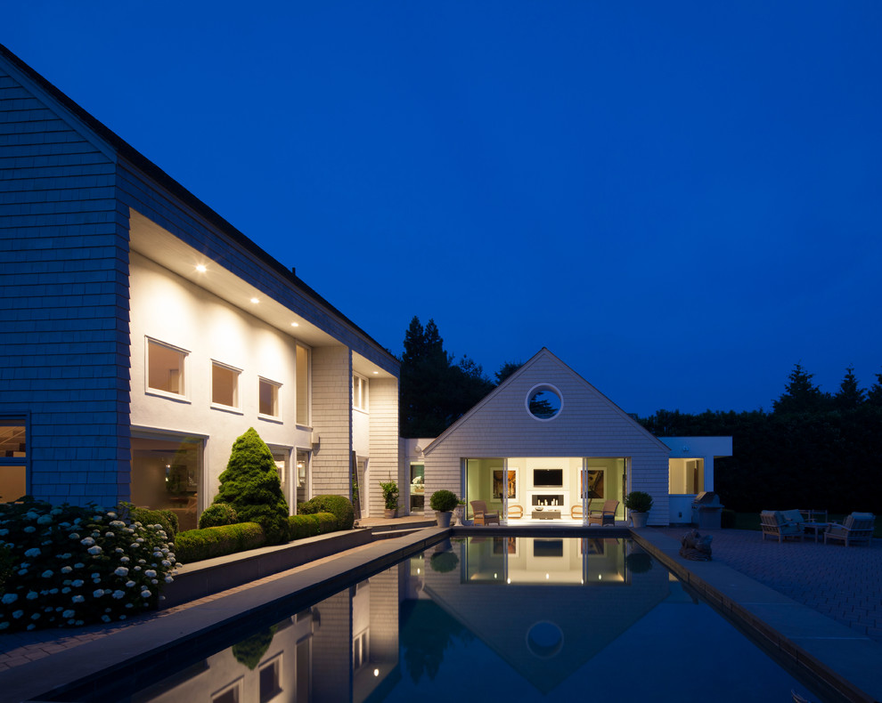 Inspiration for a large contemporary rectangular lap pool in New York with a pool house and brick pavers.
