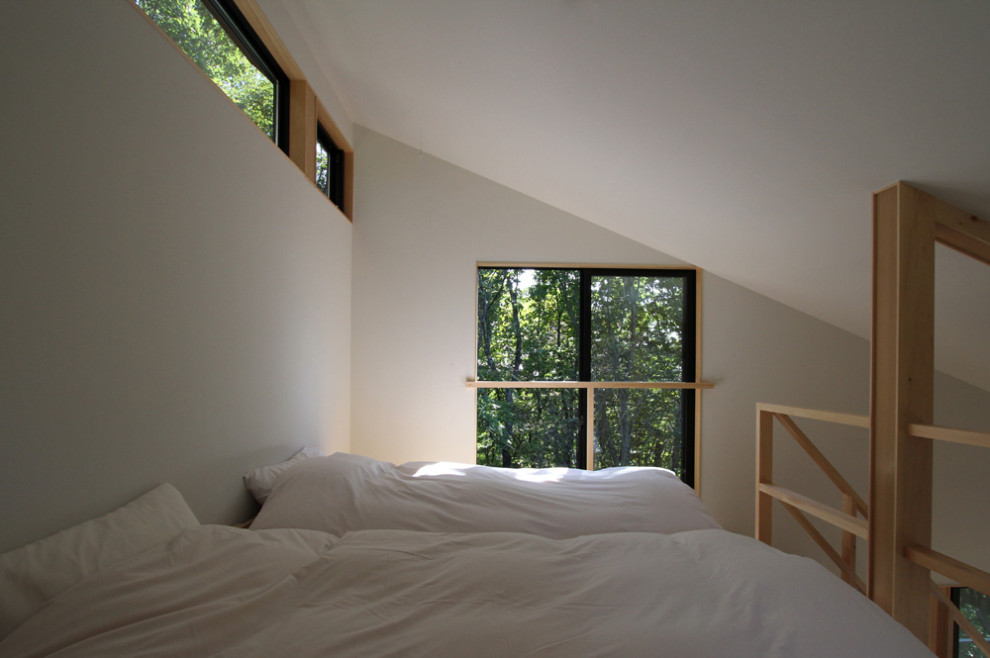 Diseño de dormitorio tipo loft y blanco moderno pequeño con paredes blancas, suelo de madera clara, chimenea de esquina y marco de chimenea de piedra