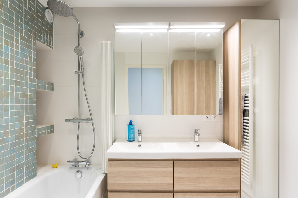 Photo of a small contemporary master bathroom in Paris with light wood cabinets, an undermount tub, white walls, flat-panel cabinets, a shower/bathtub combo, a two-piece toilet, blue tile, mosaic tile, a trough sink, solid surface benchtops, a sliding shower screen and white benchtops.