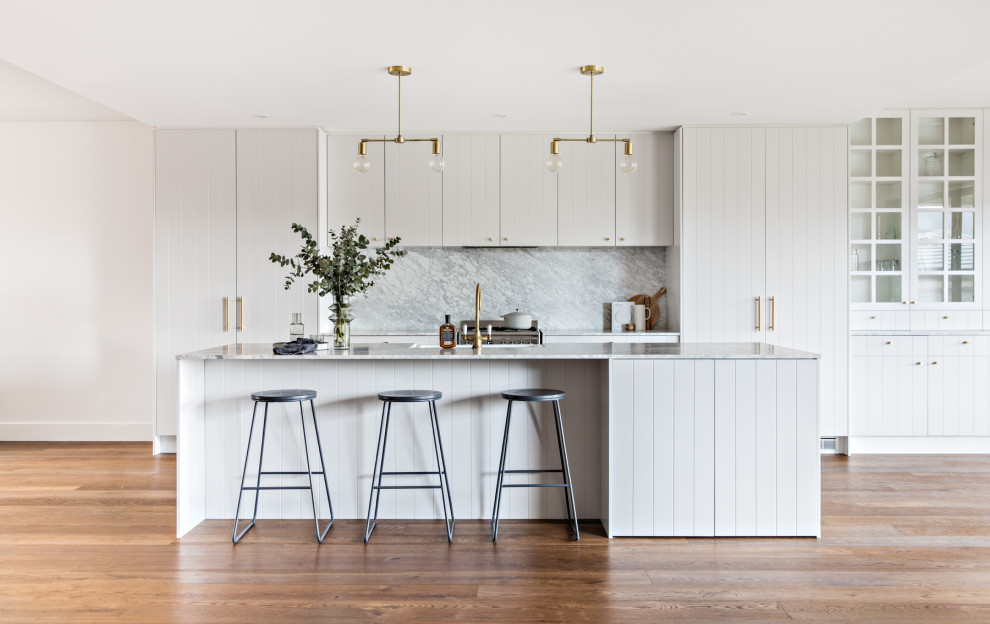 Scandinavian galley kitchen in Sydney with a farmhouse sink, flat-panel cabinets, white cabinets, grey splashback, panelled appliances, medium hardwood floors, with island, brown floor and grey benchtop.