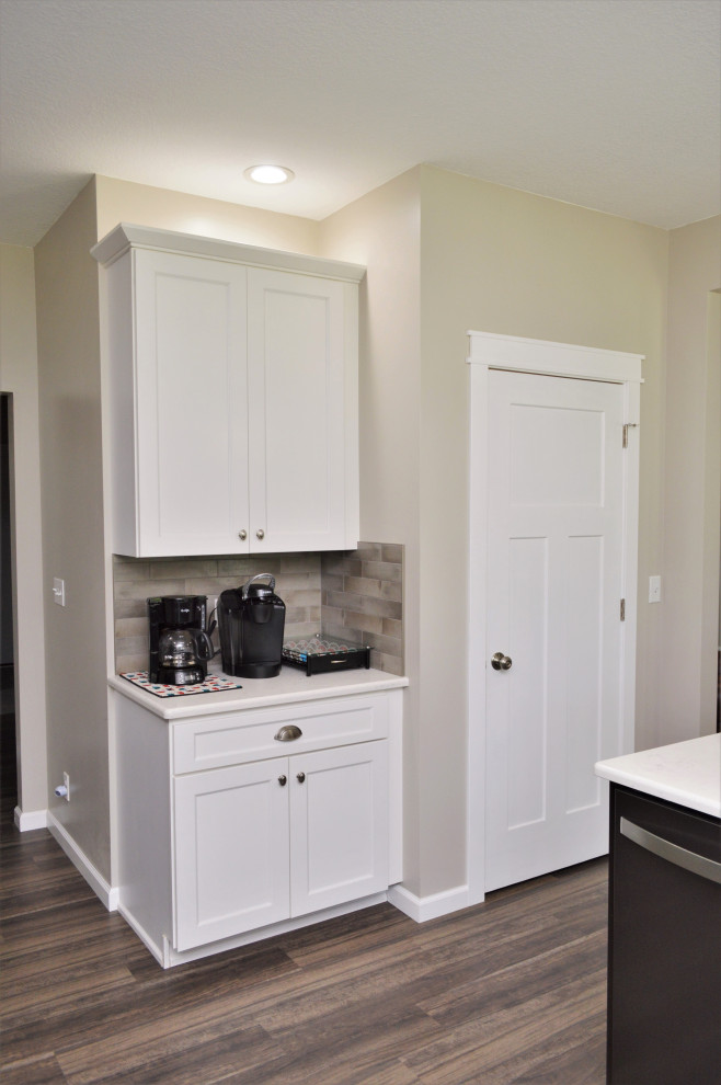 Mid-sized transitional single-wall open concept kitchen photo with a drop-in sink, shaker cabinets, white cabinets, quartzite countertops, beige backsplash, stainless steel appliances, an island and white countertops