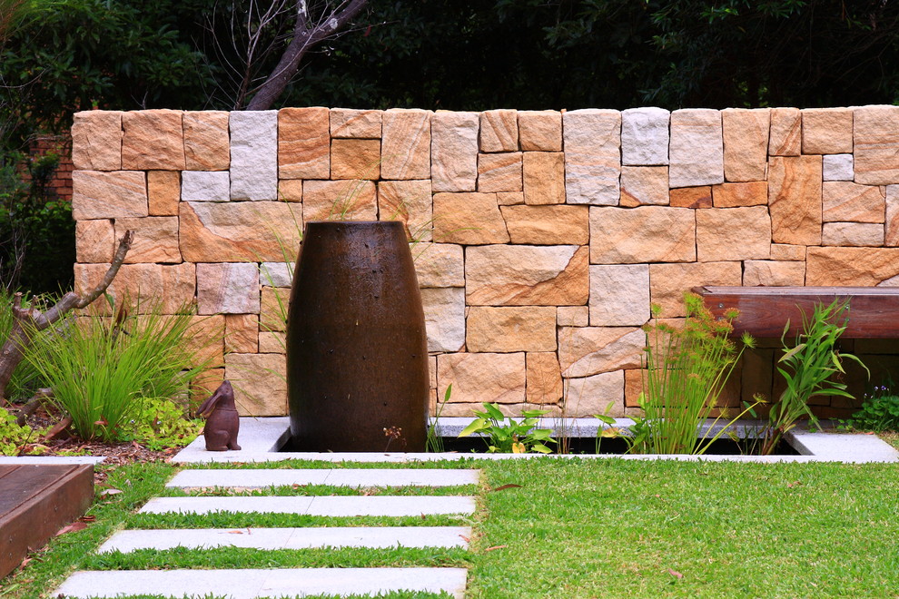 This is an example of a mid-sized modern front yard partial sun garden for summer in Sydney with a water feature and natural stone pavers.