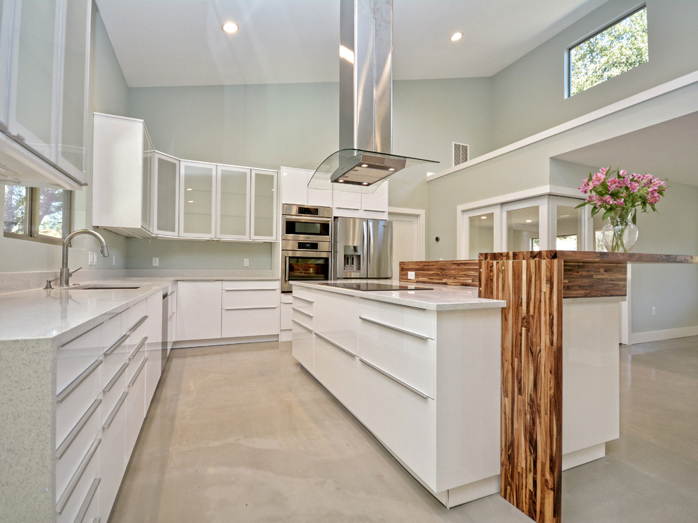 Design ideas for a mid-sized transitional l-shaped open plan kitchen in Austin with flat-panel cabinets, white cabinets, quartz benchtops, with island, an undermount sink, white splashback, stone slab splashback, stainless steel appliances and concrete floors.