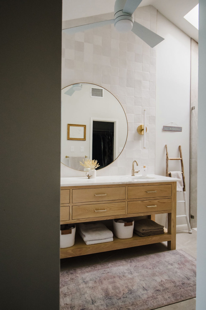 Cette image montre une salle de bain principale minimaliste en bois clair avec un placard à porte plane, une baignoire indépendante, un espace douche bain, un carrelage blanc, des carreaux de céramique, un mur blanc, un sol en carrelage de porcelaine, un lavabo encastré, un plan de toilette en marbre, un sol beige, une cabine de douche à porte battante, un plan de toilette blanc, meuble double vasque, meuble-lavabo sur pied et un plafond voûté.