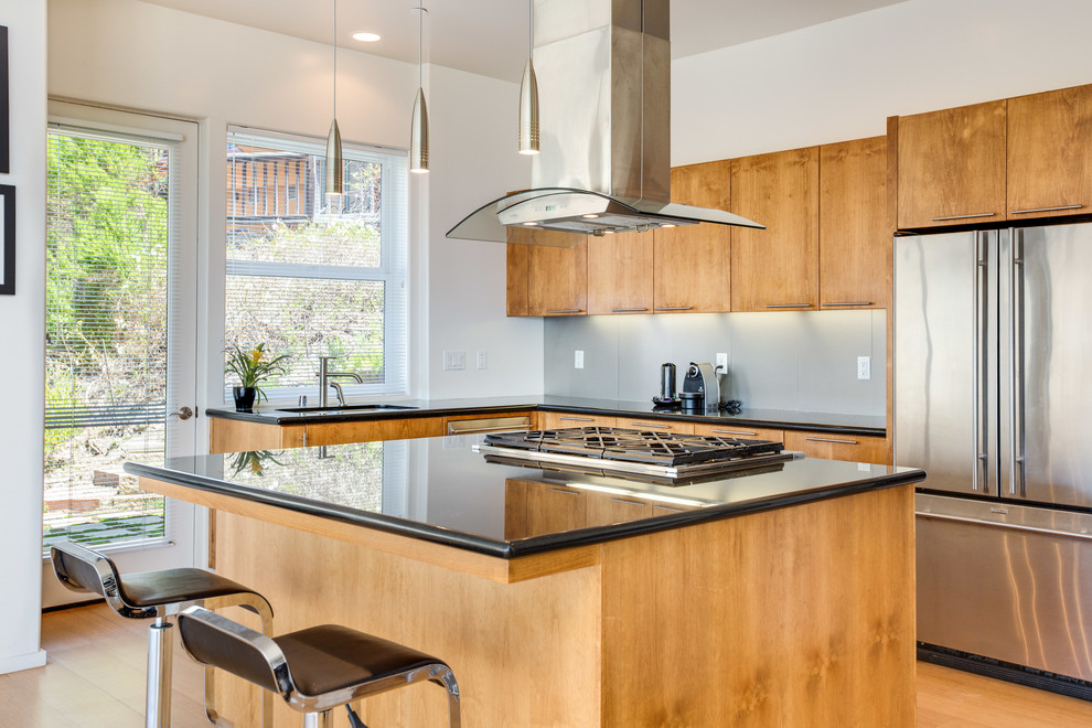 Mid-sized contemporary u-shaped open plan kitchen in San Luis Obispo with an integrated sink, flat-panel cabinets, light wood cabinets, solid surface benchtops, grey splashback, metal splashback, stainless steel appliances, light hardwood floors and with island.