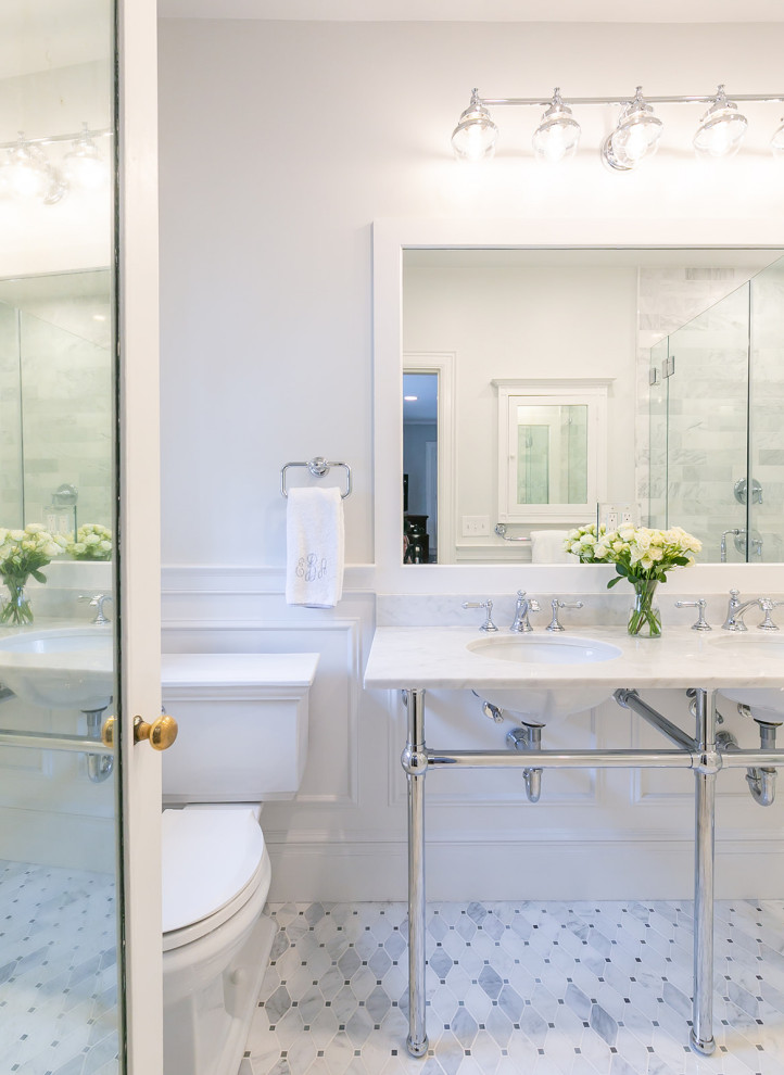 Klassisk inredning av ett vit vitt badrum, med vita skåp, en öppen dusch, en toalettstol med separat cisternkåpa, vit kakel, marmorkakel, vita väggar, marmorgolv, ett piedestal handfat, marmorbänkskiva, vitt golv och dusch med gångjärnsdörr