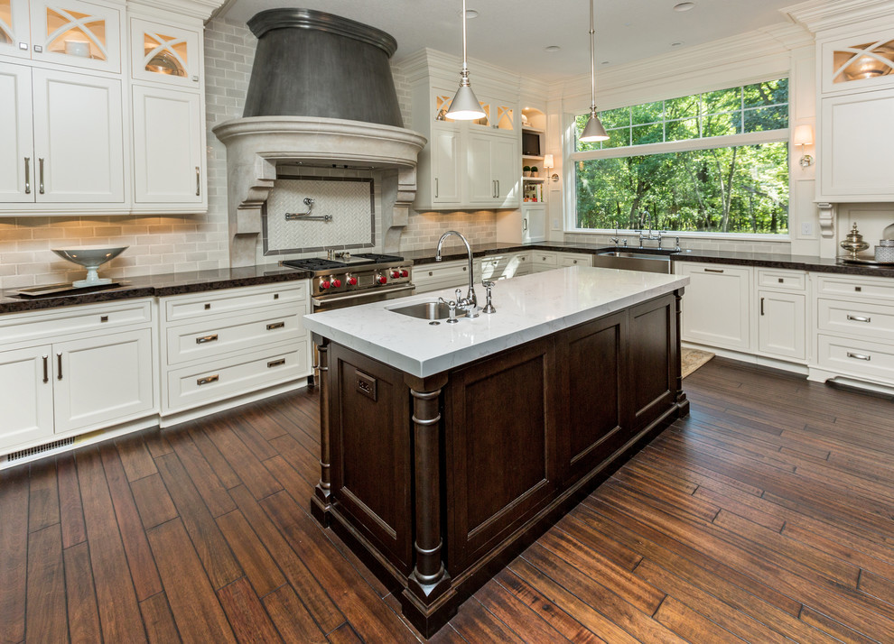 Large transitional u-shaped dark wood floor eat-in kitchen photo with shaker cabinets, two islands, a farmhouse sink, white cabinets, marble countertops, gray backsplash, subway tile backsplash and stainless steel appliances