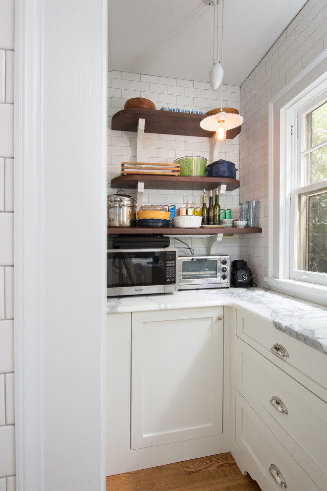 Mid-sized transitional medium tone wood floor and brown floor kitchen pantry photo in Atlanta with a farmhouse sink, shaker cabinets, white cabinets, marble countertops, white backsplash, subway tile backsplash, stainless steel appliances, an island and white countertops