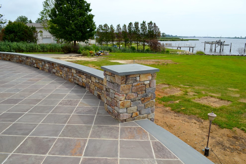 This is an example of a mid-sized beach style backyard patio in New York with natural stone pavers and no cover.
