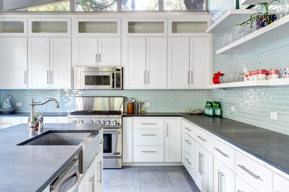 Photo of a transitional l-shaped kitchen in Austin with a farmhouse sink, shaker cabinets, white cabinets, granite benchtops, blue splashback, glass tile splashback, stainless steel appliances, porcelain floors and with island.