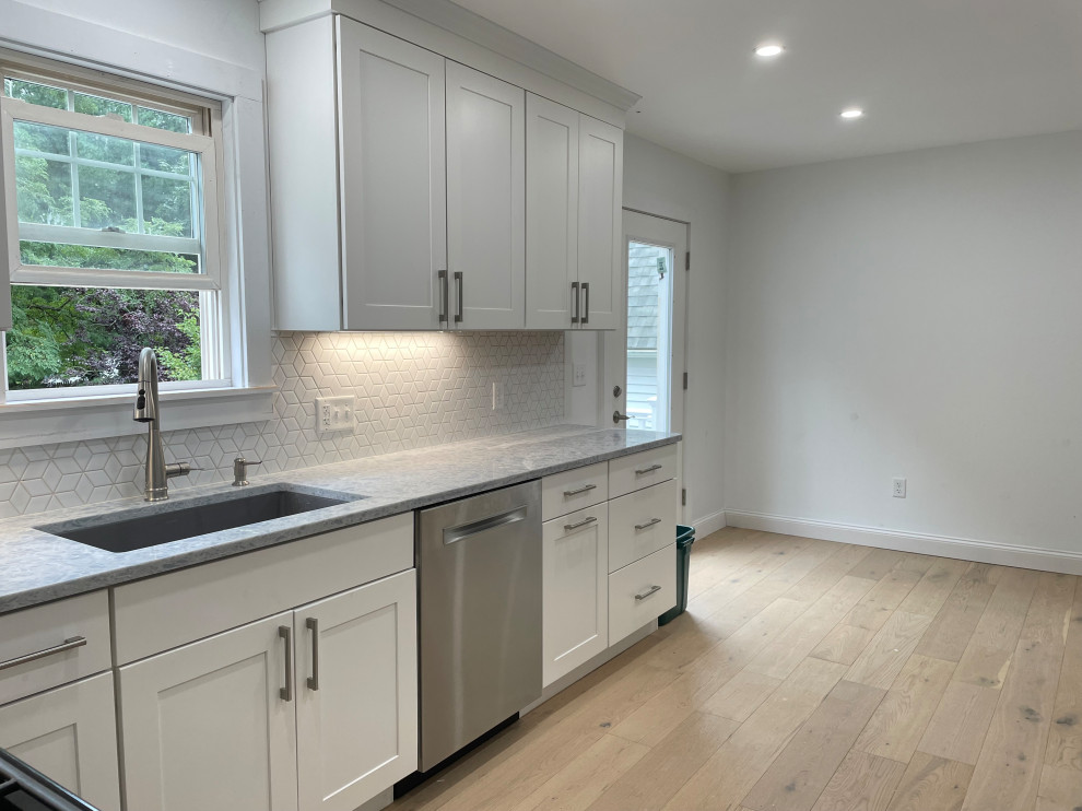Example of a large transitional l-shaped light wood floor and brown floor kitchen pantry design in Boston with an undermount sink, shaker cabinets, white cabinets, quartz countertops, white backsplash, ceramic backsplash, stainless steel appliances, no island and gray countertops