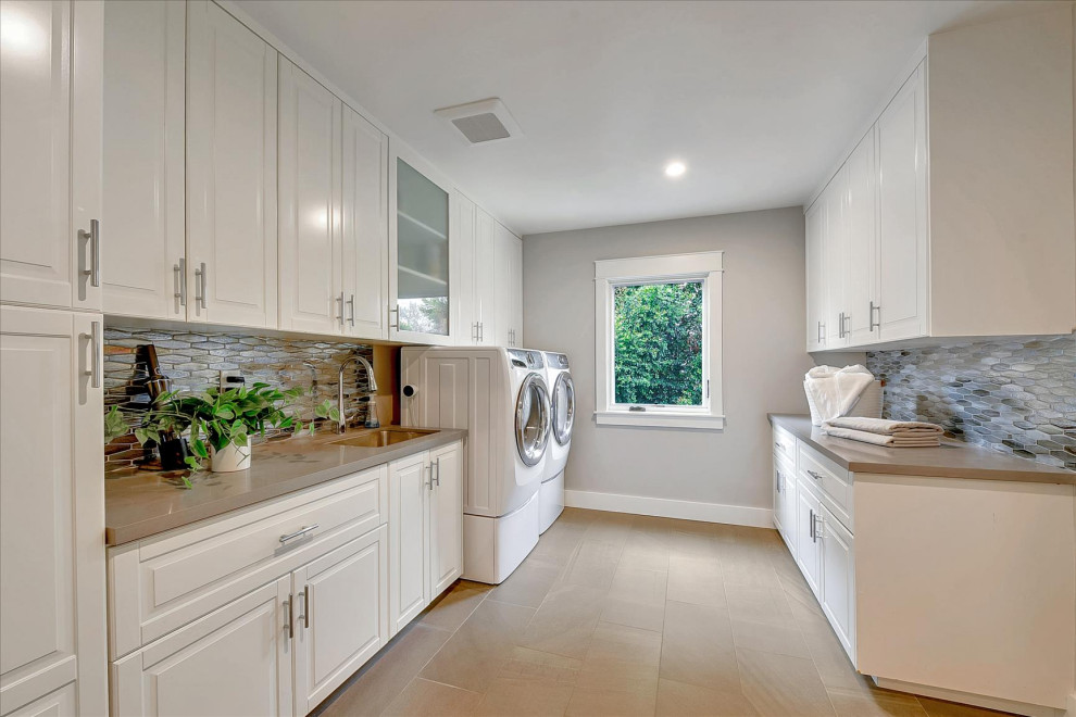Design ideas for a large arts and crafts dedicated laundry room in San Francisco with an undermount sink, raised-panel cabinets, white cabinets, quartz benchtops, multi-coloured splashback, stone tile splashback, grey walls, porcelain floors, a side-by-side washer and dryer, brown floor and grey benchtop.