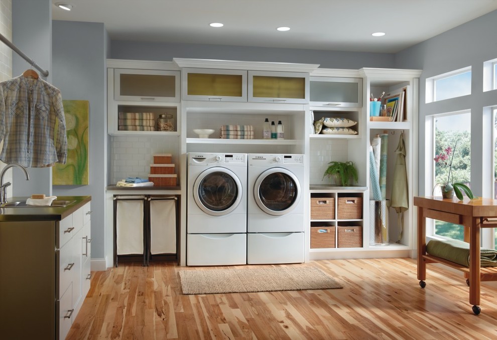 Photo of a large traditional l-shaped utility room in Other with glass-front cabinets, white cabinets, a side-by-side washer and dryer, medium hardwood floors and grey walls.