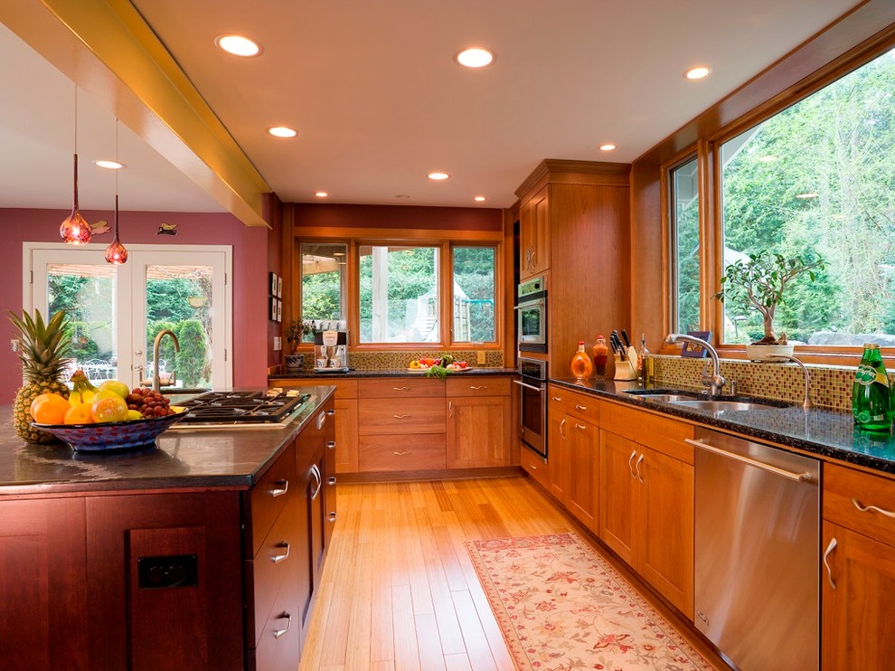 Mid-sized transitional l-shaped light wood floor eat-in kitchen photo in Seattle with an undermount sink, shaker cabinets, medium tone wood cabinets, granite countertops, multicolored backsplash, glass tile backsplash, stainless steel appliances and an island