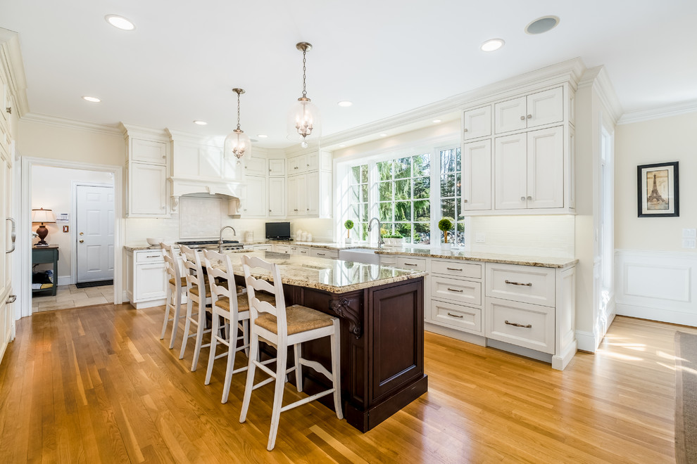Design ideas for a large traditional l-shaped eat-in kitchen in Bridgeport with a farmhouse sink, beaded inset cabinets, white cabinets, granite benchtops, white splashback, subway tile splashback, panelled appliances, medium hardwood floors, with island and beige benchtop.
