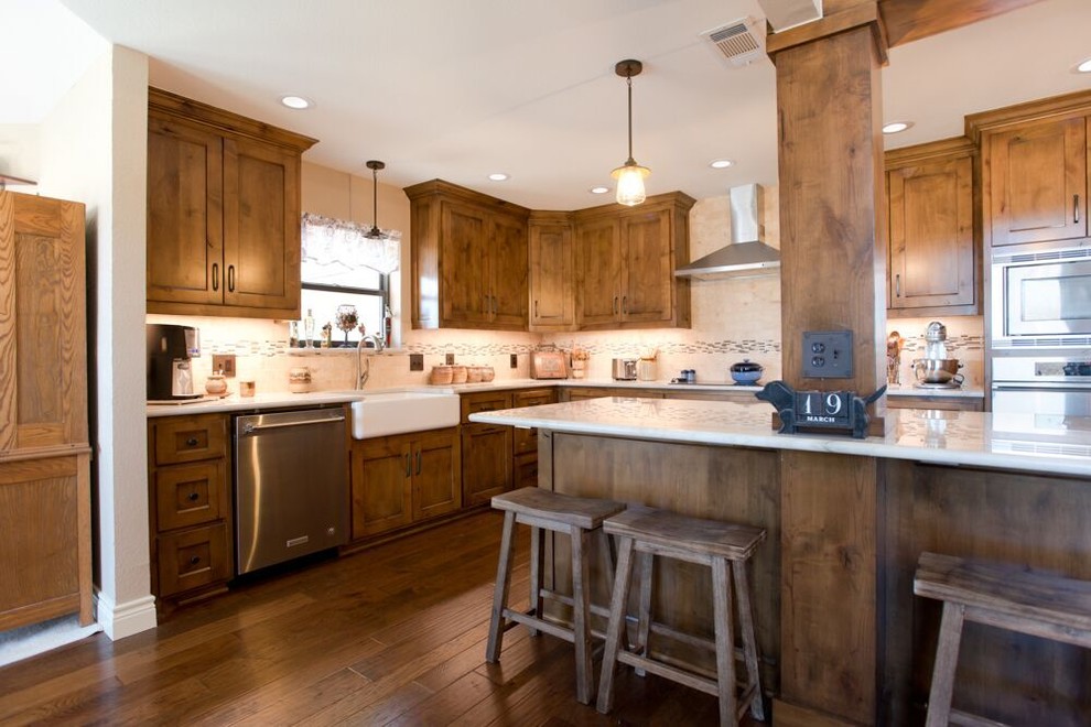 Inspiration for a large transitional l-shaped brown floor and medium tone wood floor eat-in kitchen remodel in Dallas with a farmhouse sink, recessed-panel cabinets, medium tone wood cabinets, multicolored backsplash, an island, quartzite countertops, travertine backsplash, stainless steel appliances and white countertops