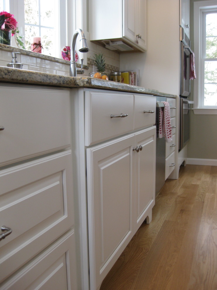 Inspiration for a transitional u-shaped medium tone wood floor eat-in kitchen remodel in Boston with an undermount sink, raised-panel cabinets, white cabinets, granite countertops, white backsplash, ceramic backsplash, stainless steel appliances, an island and beige countertops