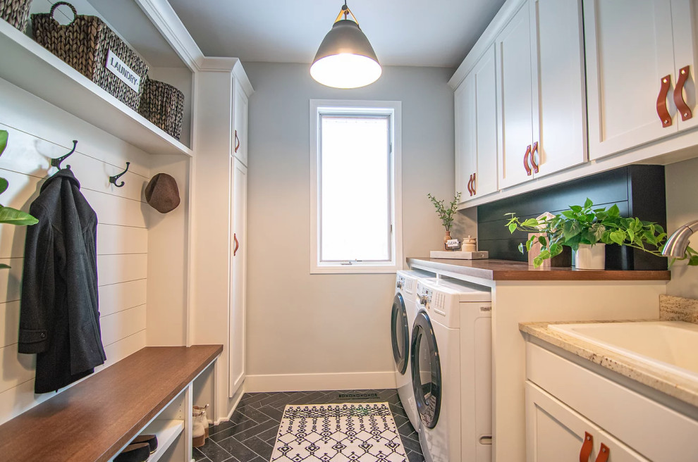 Photo of a mid-sized transitional laundry room in Minneapolis with an utility sink, shaker cabinets, white cabinets, wood benchtops, slate splashback, slate floors, a side-by-side washer and dryer, black floor and brown benchtop.