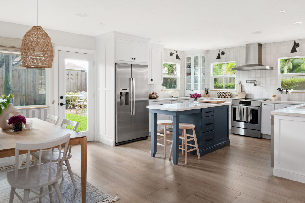 Example of a mid-sized beach style u-shaped medium tone wood floor and brown floor eat-in kitchen design in Tampa with an undermount sink, shaker cabinets, white cabinets, quartz countertops, white backsplash, porcelain backsplash, stainless steel appliances, an island and white countertops