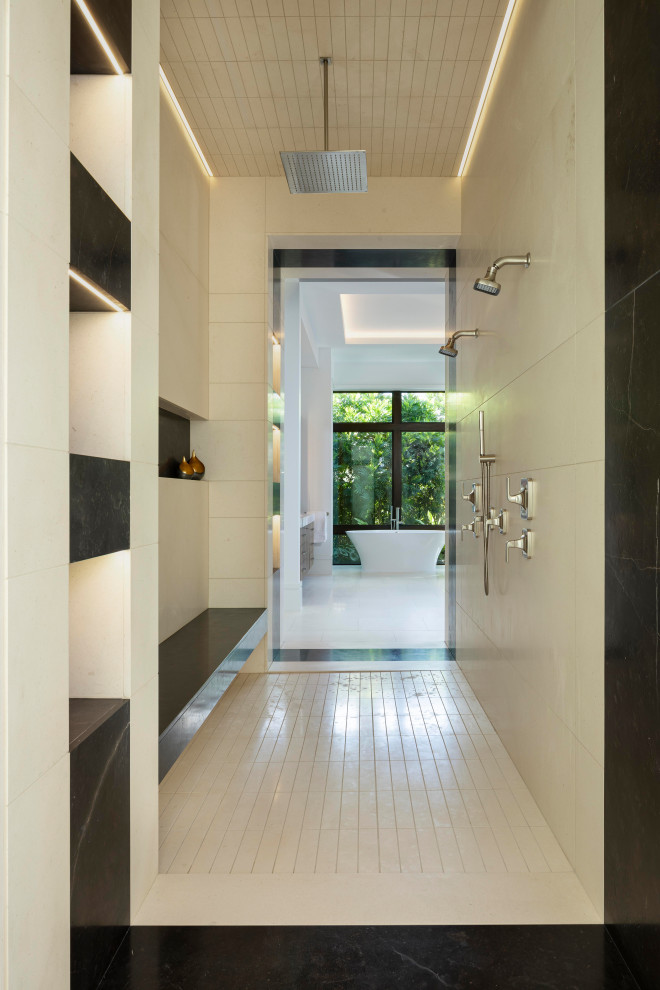 This is an example of a large mediterranean master bathroom with flat-panel cabinets, medium wood cabinets, a freestanding tub, an open shower, a wall-mount toilet, black and white tile, limestone, white walls, limestone floors, an undermount sink, marble benchtops, white floor, an open shower, a shower seat, a double vanity, a built-in vanity, recessed and wood walls.