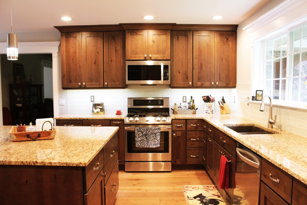 Open concept kitchen - large rustic u-shaped light wood floor and brown floor open concept kitchen idea in Boise with an undermount sink, shaker cabinets, brown cabinets, granite countertops, white backsplash, glass tile backsplash, stainless steel appliances and an island