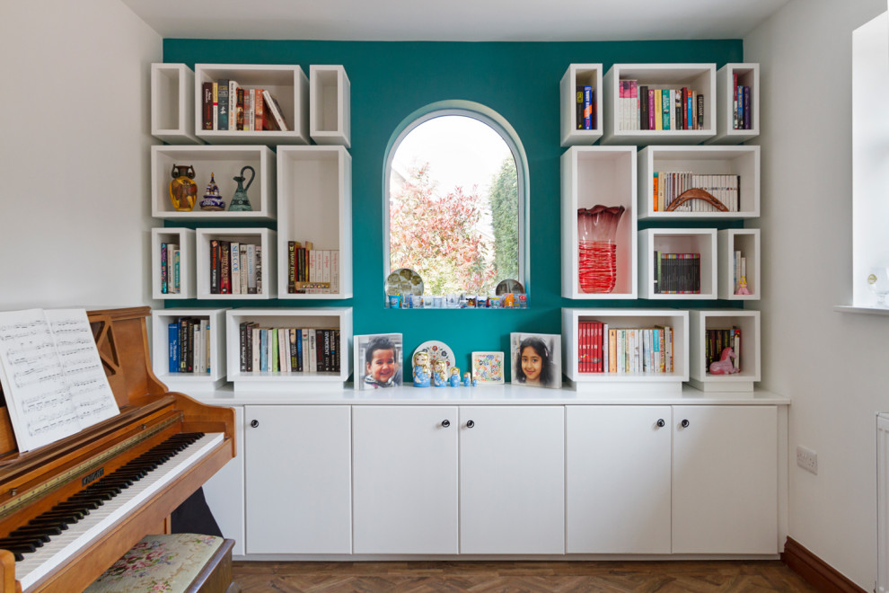 This is an example of a mid-sized contemporary home office in West Midlands with blue walls, dark hardwood floors, a two-sided fireplace, a plaster fireplace surround and brown floor.