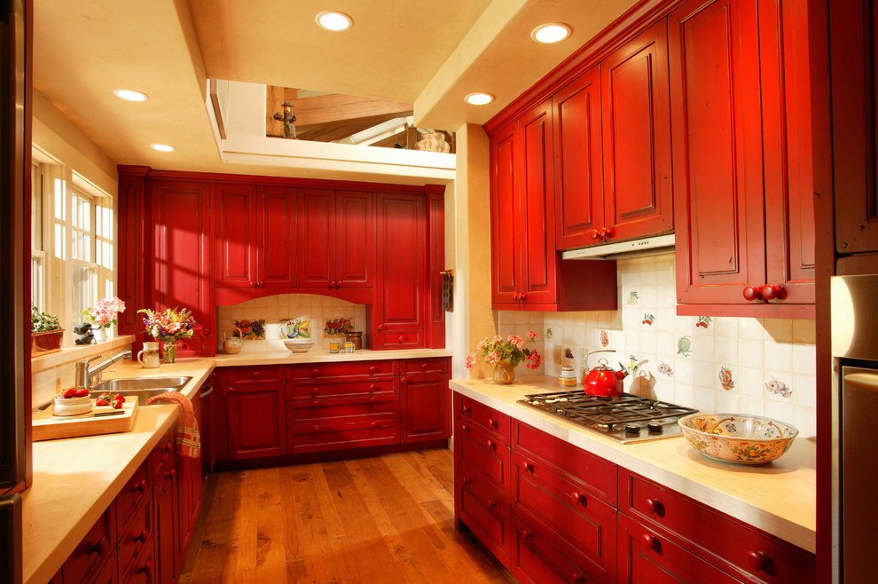 Design ideas for a mid-sized country galley kitchen in Denver with a drop-in sink, raised-panel cabinets, red cabinets, ceramic splashback, stainless steel appliances, medium hardwood floors, beige splashback and with island.