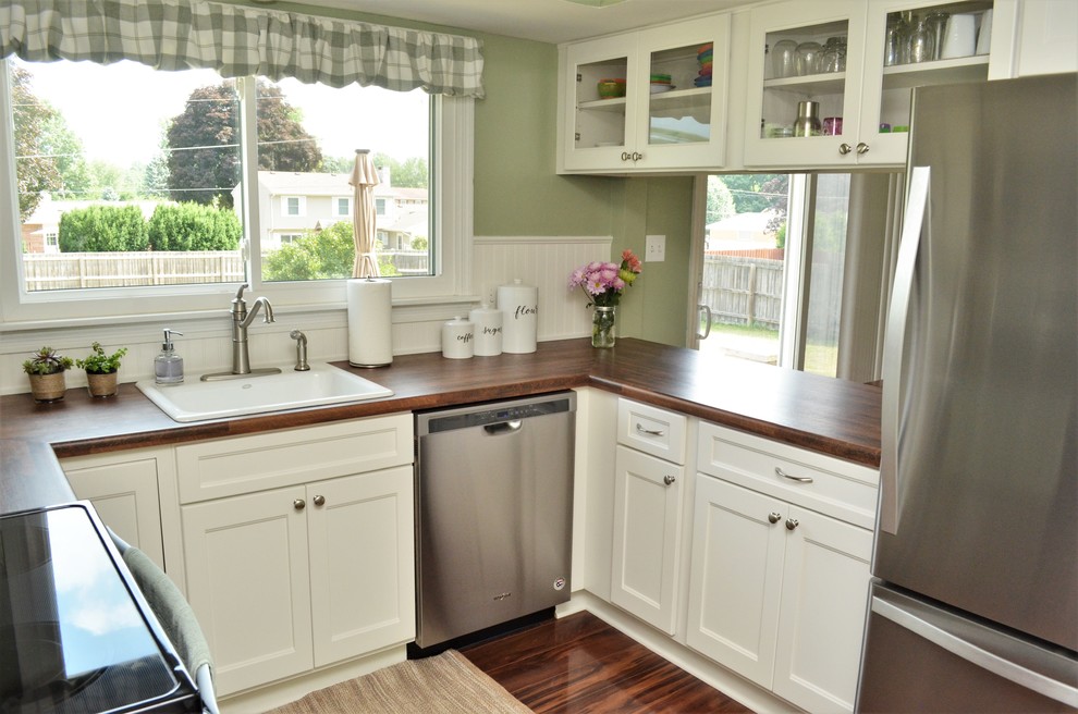 Photo of a mid-sized country u-shaped eat-in kitchen in Other with a drop-in sink, shaker cabinets, white cabinets, laminate benchtops, white splashback, timber splashback, stainless steel appliances, a peninsula, brown floor and brown benchtop.