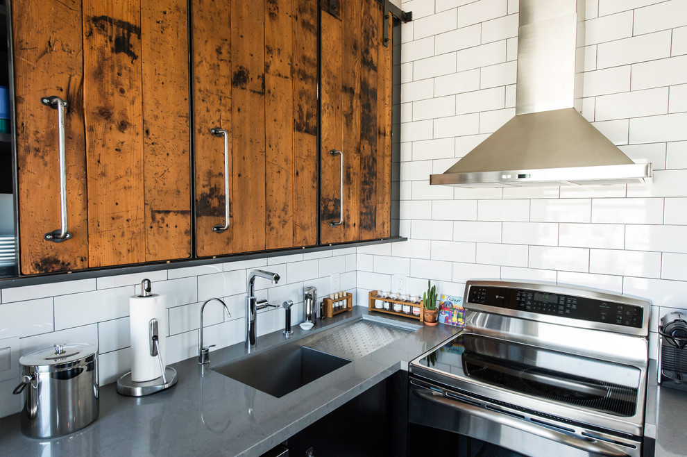 Inspiration for a mid-sized industrial u-shaped separate kitchen in San Francisco with an undermount sink, flat-panel cabinets, black cabinets, quartz benchtops, white splashback, subway tile splashback, stainless steel appliances and a peninsula.