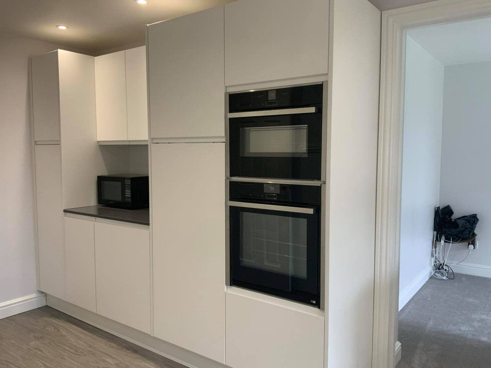 Inspiration for a large contemporary l-shaped eat-in kitchen in Buckinghamshire with flat-panel cabinets, white cabinets, quartzite benchtops, black splashback, engineered quartz splashback, panelled appliances, vinyl floors, a peninsula, brown floor and black benchtop.