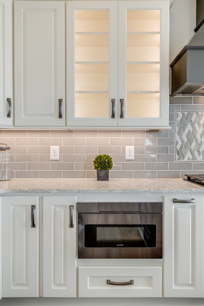 Example of a large transitional l-shaped open concept kitchen design with an undermount sink, raised-panel cabinets, white cabinets, quartz countertops, gray backsplash, subway tile backsplash, stainless steel appliances, an island and white countertops