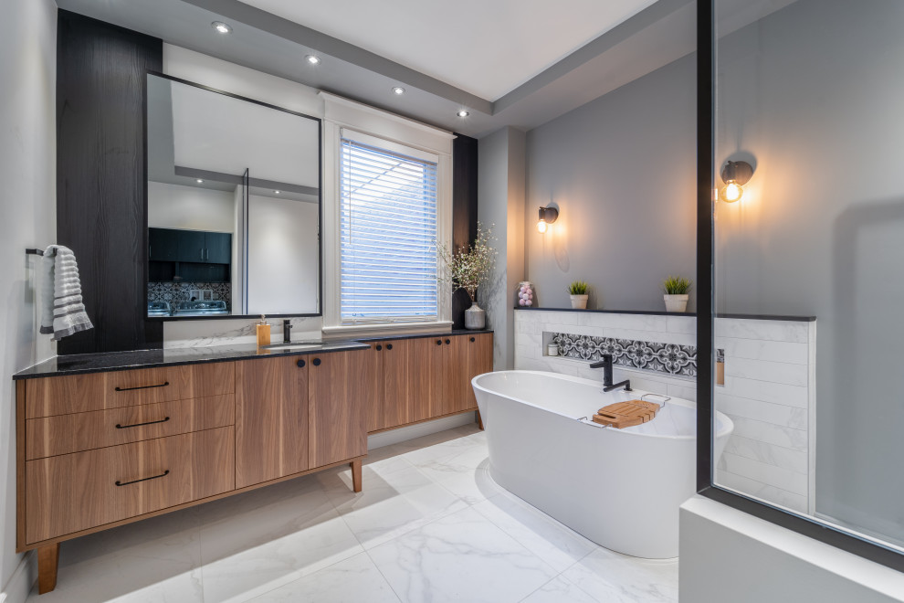This is an example of a contemporary master bathroom in Montreal with flat-panel cabinets, brown cabinets, a freestanding tub, an open shower, black and white tile, gray tile, grey walls, marble floors, an undermount sink, engineered quartz benchtops, multi-coloured floor, an open shower, black benchtops, a single vanity and a built-in vanity.