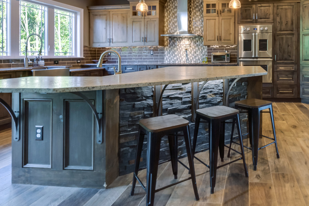 Photo of a large country l-shaped open plan kitchen in Philadelphia with a farmhouse sink, raised-panel cabinets, distressed cabinets, quartz benchtops, grey splashback, cement tile splashback, stainless steel appliances, porcelain floors, with island and brown floor.