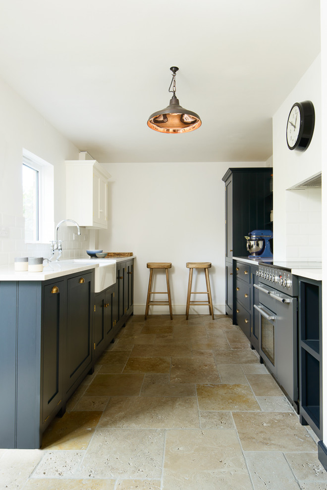 Small country galley separate kitchen in Other with a farmhouse sink, shaker cabinets, blue cabinets, solid surface benchtops, white splashback, subway tile splashback, black appliances, travertine floors and no island.