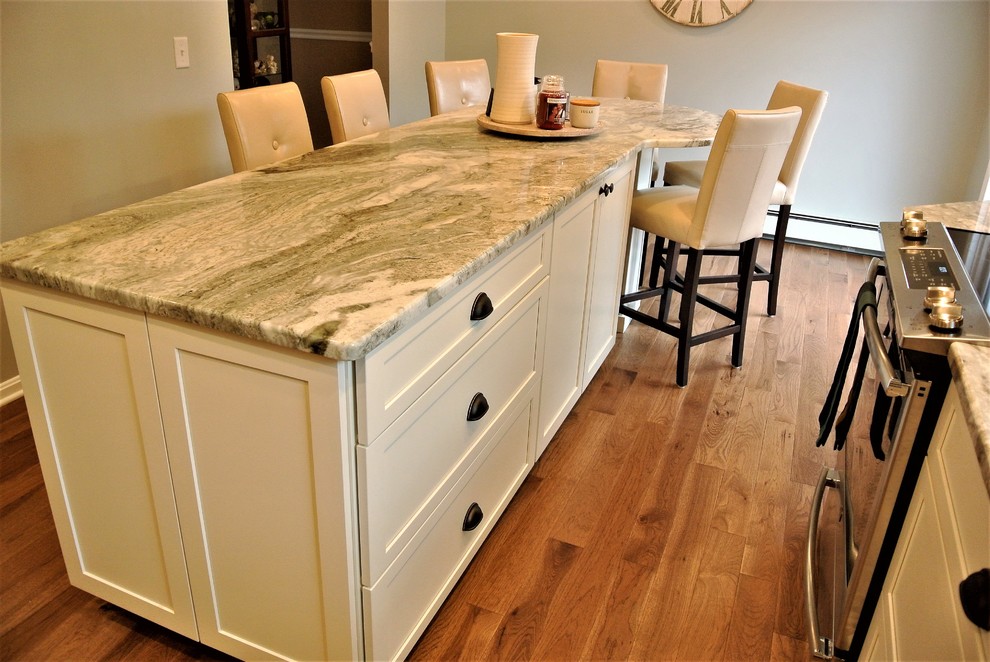 Inspiration for a transitional l-shaped medium tone wood floor kitchen remodel in Boston with an undermount sink, shaker cabinets, white cabinets, granite countertops, beige backsplash, subway tile backsplash, stainless steel appliances and an island