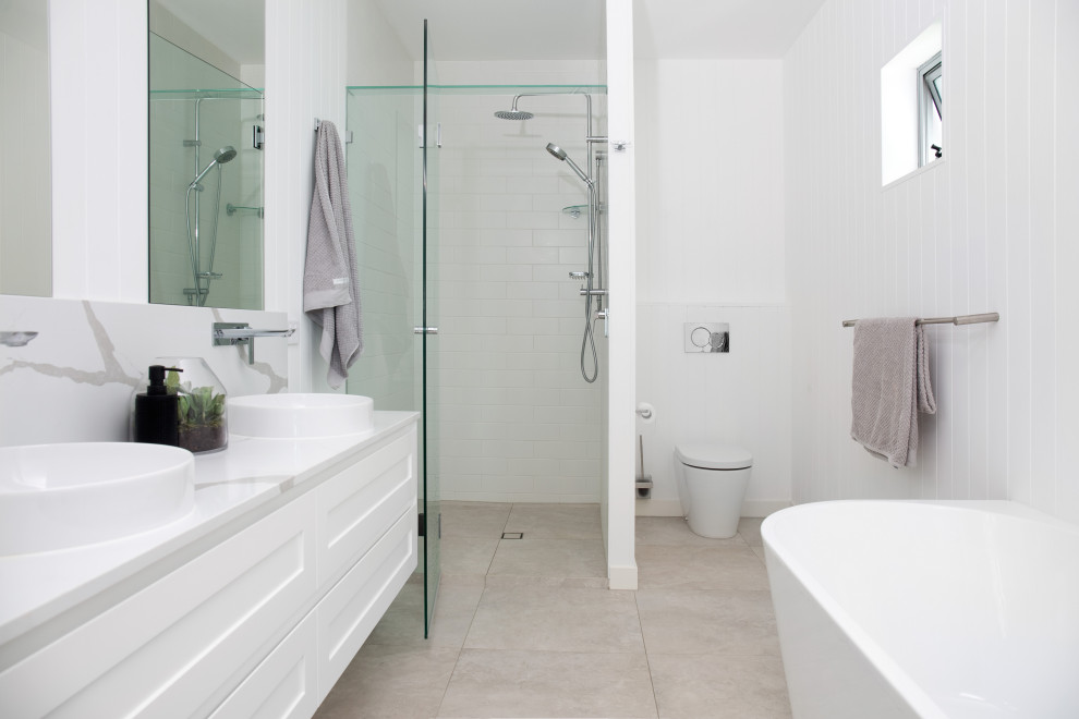 Mid-sized transitional master bathroom in Brisbane with shaker cabinets, white cabinets, a freestanding tub, an alcove shower, white tile, porcelain tile, grey walls, porcelain floors, a hinged shower door, white benchtops, a double vanity, a floating vanity, beige floor and panelled walls.