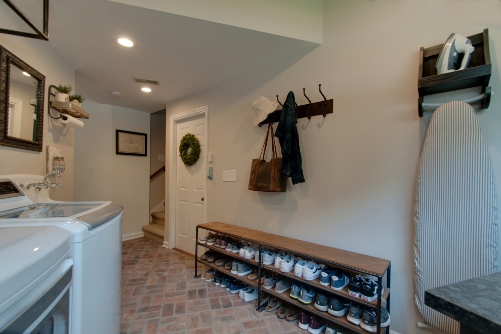 Photo of a small country utility room in Nashville with a farmhouse sink, shaker cabinets, brown cabinets, granite benchtops, grey walls, brick floors, a side-by-side washer and dryer, multi-coloured floor and black benchtop.